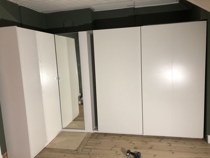 Nybyggda vita garderober i ett oinrett sovrum med trägolv och ett verktyg på golvet.