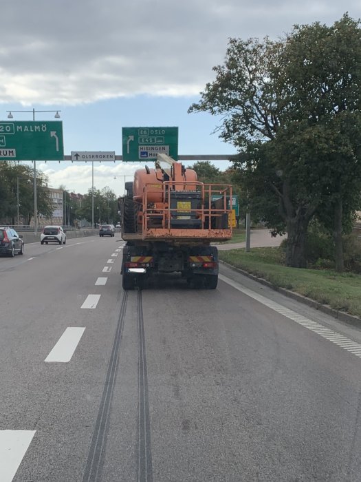 Lastbil som transporterar en stor orange tank på en väg med trafikskyltar som pekar mot Malmö och Oslo.