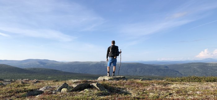 Man står på en klippa och blickar ut över ett vidsträckt fjällandskap, symboliserar minnen och arv från en älskad plastmormor.