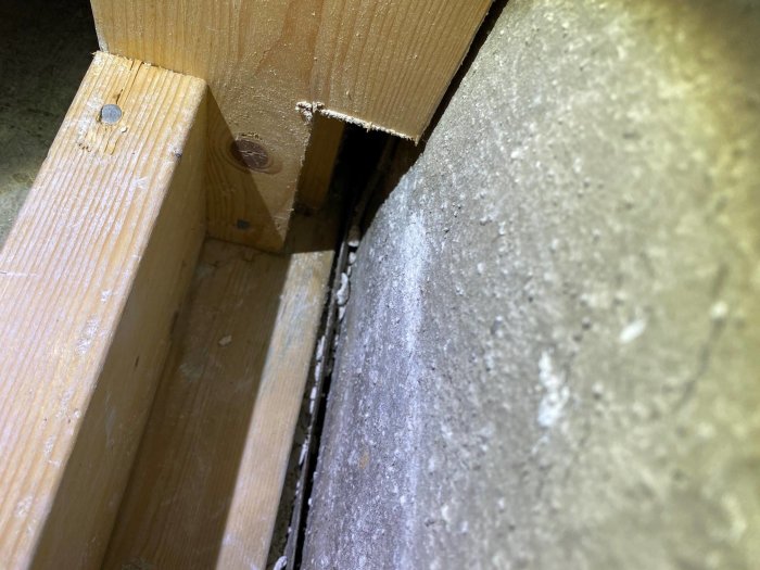 Träregel som inte är gjuten i betongplattan utan står på en sula med fiber- eller asfaltmatta under, i ett renoverat källarbadrum.