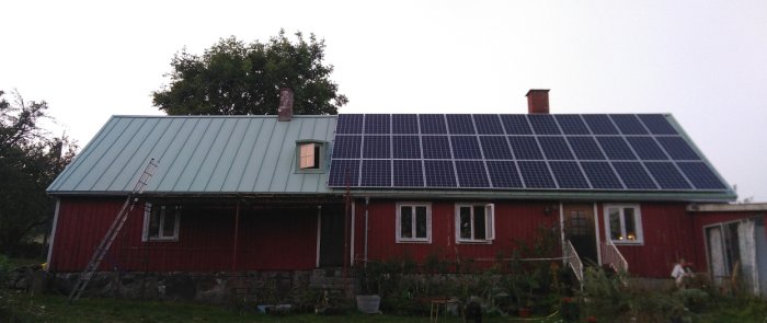 Rött hus med nytt plåttak och solcellspaneler, liten kupa och stege lutad mot fasaden.