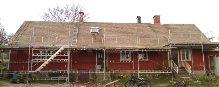 Rödfärgat hus i två våningar under takomläggning med byggnadsställningar, gammalt tak och en stege som leder upp till taket.