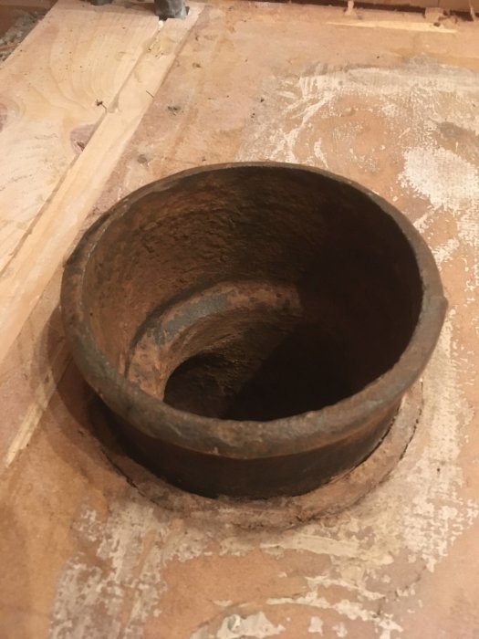 Gammalt järnavloppsrör med ytrost synligt, omgivet av spånskivor under renovering.