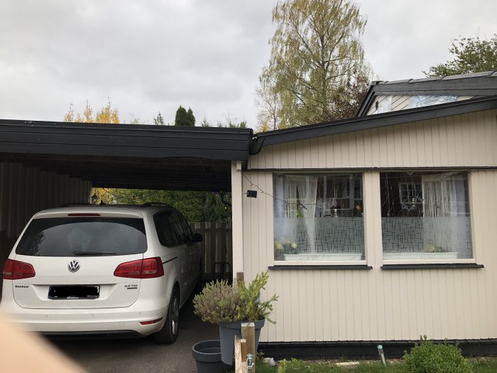 Bilparkering under carport ihopbyggd med husets altan, synliga vattenläckageproblem vid takanslutning.