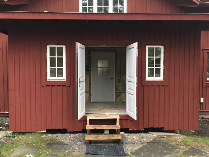 Entré till rödmålad byggnad med öppna vita dörrar och en ofärdig trappa utan avsats.