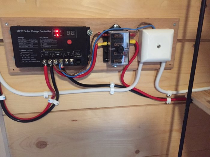 Installation av ett MPPT solcellsreglersystem med kablar och säkringsdosa på en trävägg.