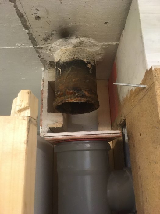 En gammal rostig avloppsrör ovanför en nyare plastavloppsrör i en källare under renovering.