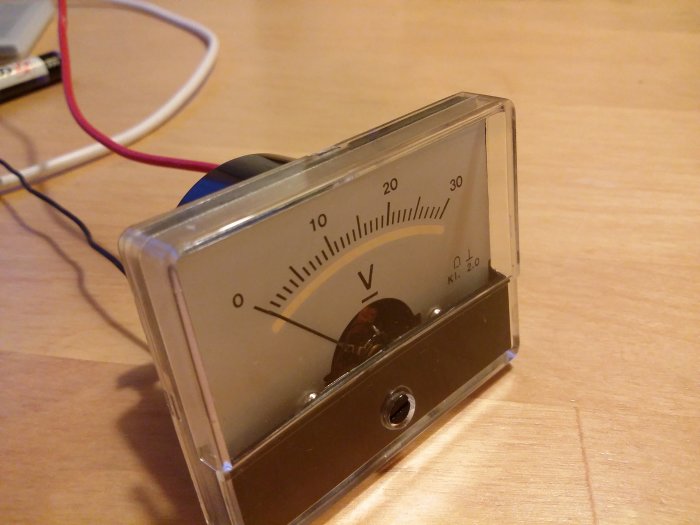 Analog voltmeter med skala upp till 30 V och anslutna kablar på ett bord.