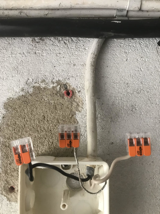 Elinstallation med öppen dosa, svart och vit kabel kopplade till skruvplintar, och oisolerad jordkabel.