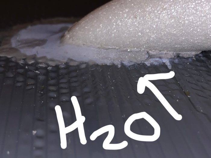 Bakre delen av en frys med kondens och vattenansamling, texten "H2O" pekar på fukten.