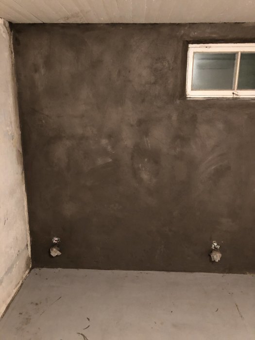 Nyligen tunnputsad vägg med ojämn yta och synlig underliggande färg nära hörn och runt fönster.