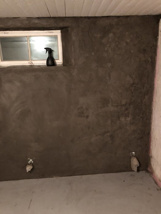 Nyligen tunnputsad vägg med ojämn yta och en blomspruta på fönsterbrädan.