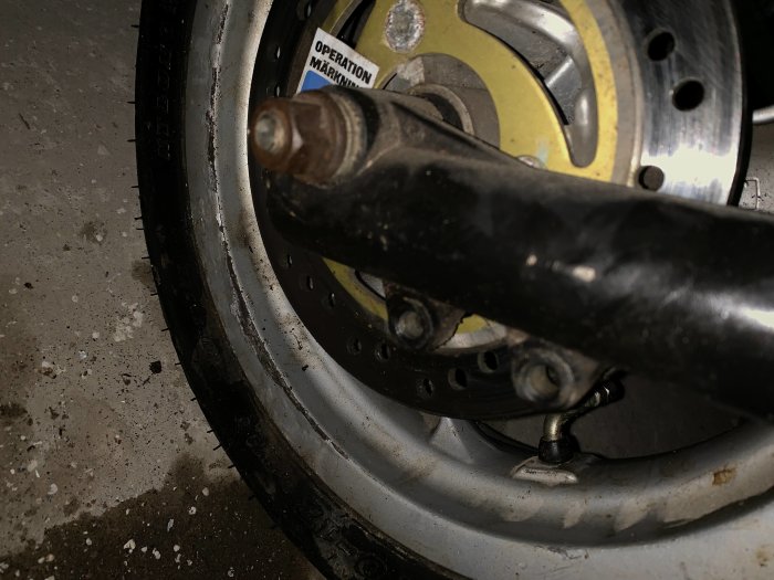 Närbild av motorcykels bromsok och skivbroms på slitet motorcykeldäck.