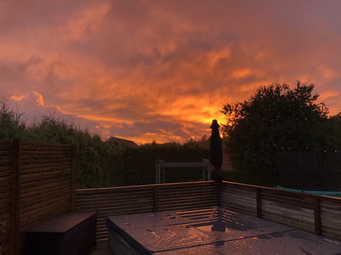 Solnedgång med brandgul himmel över ett trädgårdsdäck med bubbelpool och trampolin.