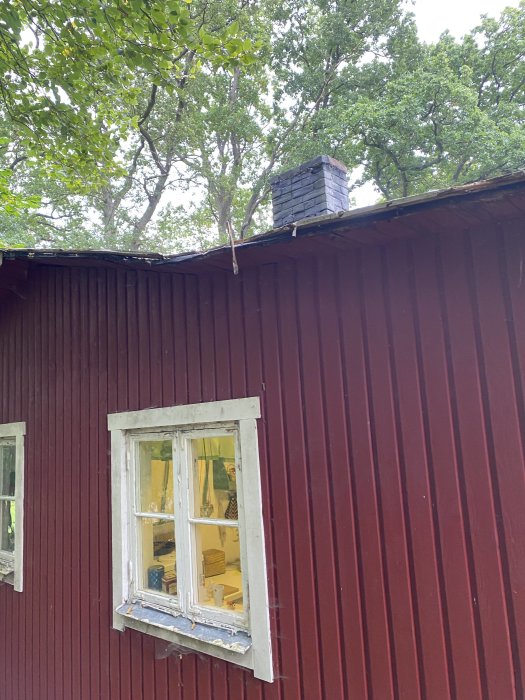 Röd fritidsstuga med oliklutande papptak och luftningsrör över tillbyggnad.