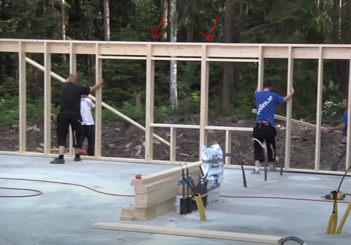 Personer som arbetar med att bygga en trästomme för fönsterinstallation på en byggplats omgiven av skog.