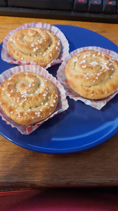 Tre nyligen uppvärmda vaniljbullar på ett blått fat med sockerdekoration.