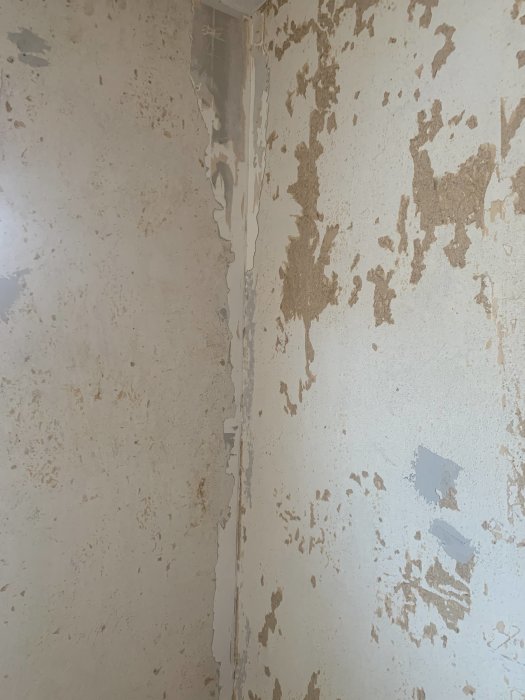 Vägg med avlägsnad tapet och synligt spackel i hörnet samt bruna rester.