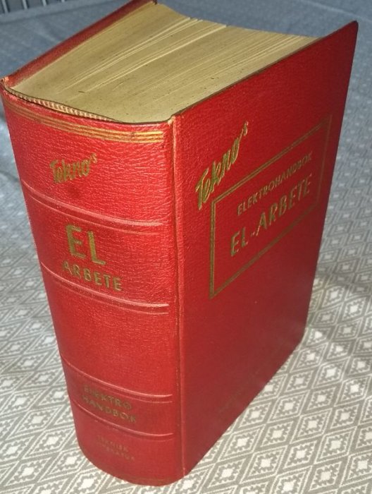 Röd bok med titeln "Tekno's Elektrohandbok El-arbete" på omslaget, stående på ett mönstrat underlag.