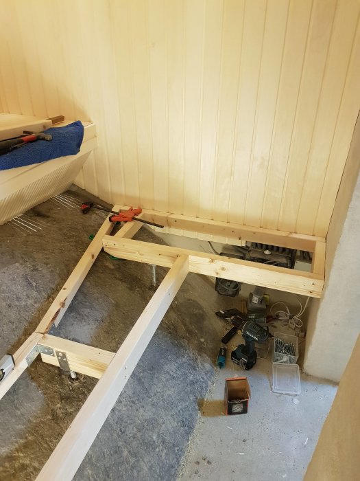 Närbild på en halvfärdig bastulave under konstruktion med trästöd, verktyg och byggmaterial.