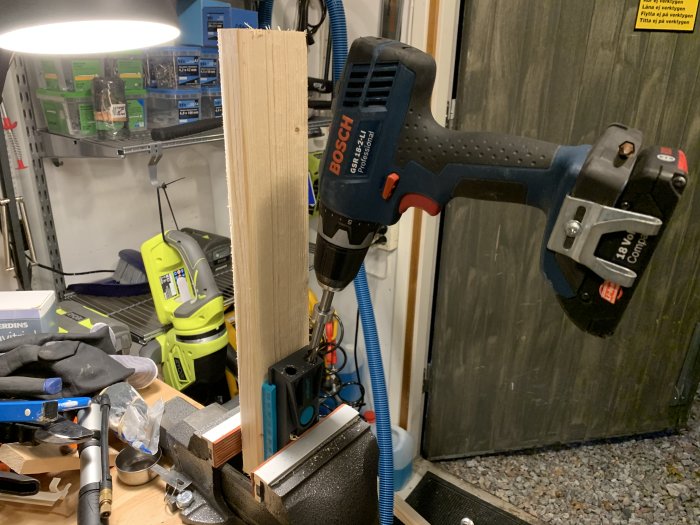 Pocket hole jig fäst vid ett trästycke i en verkstad, med en Bosch borrskruvdragare och olika verktyg i bakgrunden.