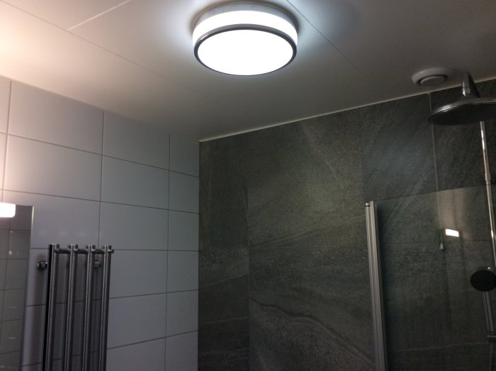 Takplafond och skåpbelysning i ett badrum med grå kakelväggar, överväger installation av spotlights.
