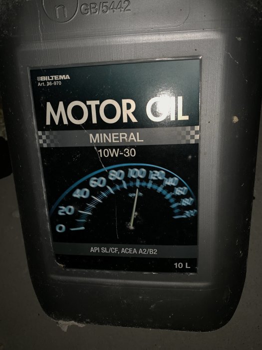 Försluten behållare av Biltema Motorolja Mineral 10W-30 med mätare, hittad bredvid en moped i garage.