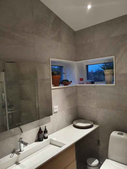 Ett modernt badrum med grå kakelväggar, handfat, spegel och dusch.