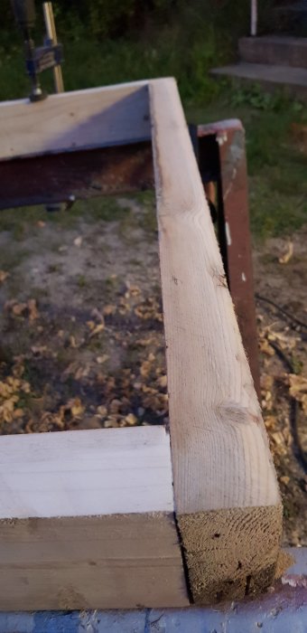 Trähörn av en skorstenskronas gjutform med avfasade kanter fastklämd i ett skruvstäd vid skymning.