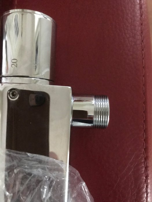 Ny duschblandare med synlig gängad anslutningsmutter i plastförpackning mot röd bakgrund.