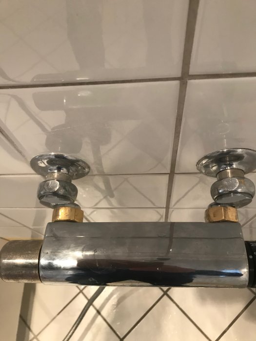 Gammal duschblandare monterad på kakelvägg med synliga anslutningsmuttrar och rör.