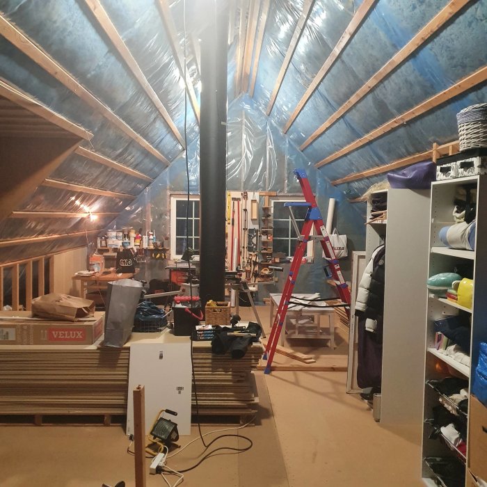 Pågående övervåningsbygge med öppen takkonstruktion, isoleringsmaterial, byggmaterial och en stege.