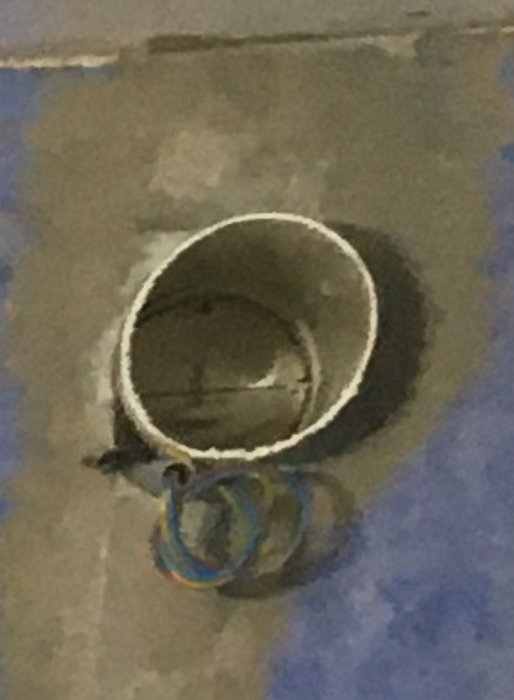 Zoomad bild på ett avkapad rör i en vägg med eltejp och slang synlig inuti.