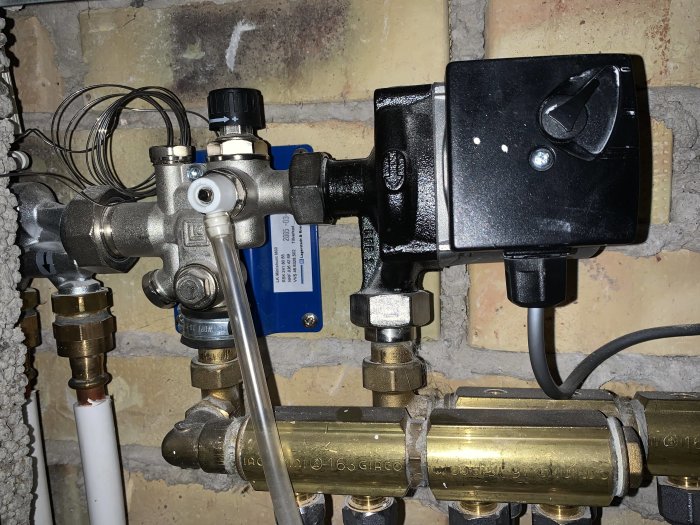 Vattenburna golvvärmekomponenter med kopplingar, ventiler och reglage monterade på en stenvägg.