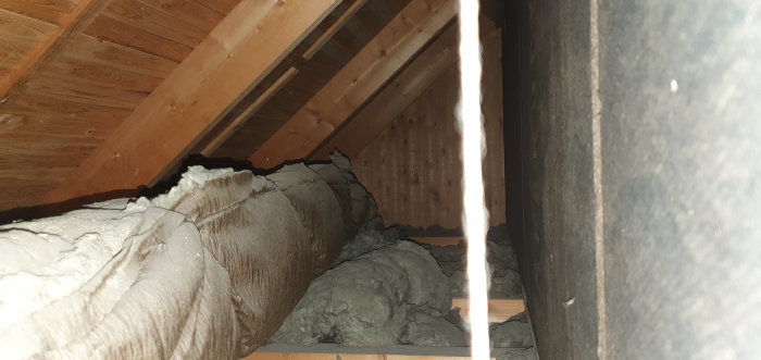 Inblick i takutrymme med stående furupanel och isolering lindad med ståltråd.