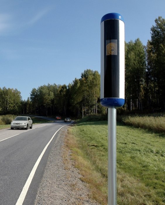 Fartkamera vid vägkanten med passerande bilar i dagsljus.