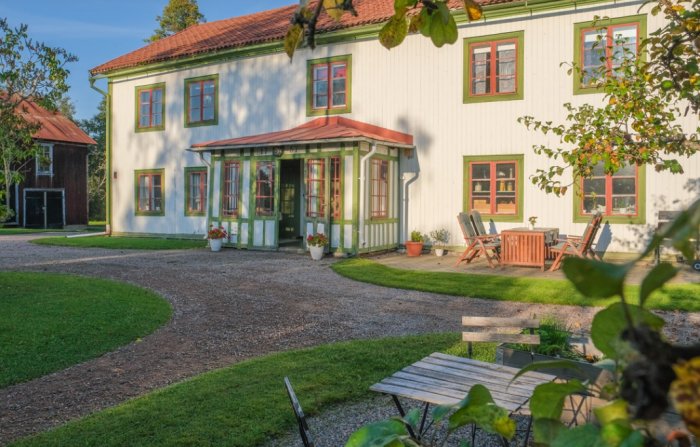 Vit traditionell tvåvåningsvilla med gröna fönsterluckor, veranda, grusgång och trädgårdsmöbler.