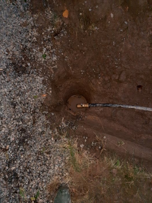 Vy av ett grävt hål i marken med PRK-rörinstallation och plastkoppling synlig ovanför jordytan.