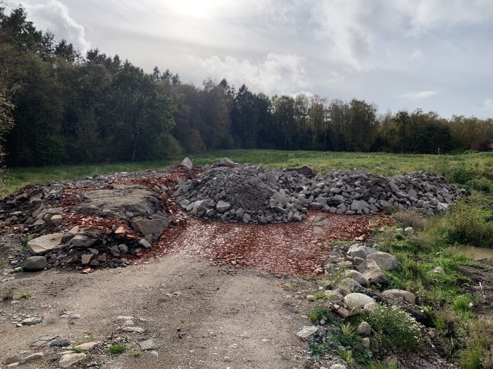 Högar av grus och sten på en framtida byggplats med träd i bakgrunden.