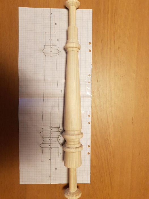 Svarvat träben bredvid en ritning på millimeterpapper, som visar design och mått för benet.