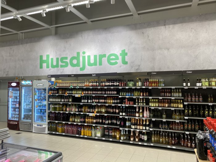 Interiör av mataffär med texten "Husdjuret" ovanför hyllor fulla med drycker.