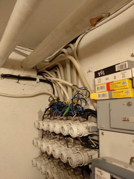 Elektriska installationer med rör och kablar som går in i en vägg ovanför en elkabelcentral.