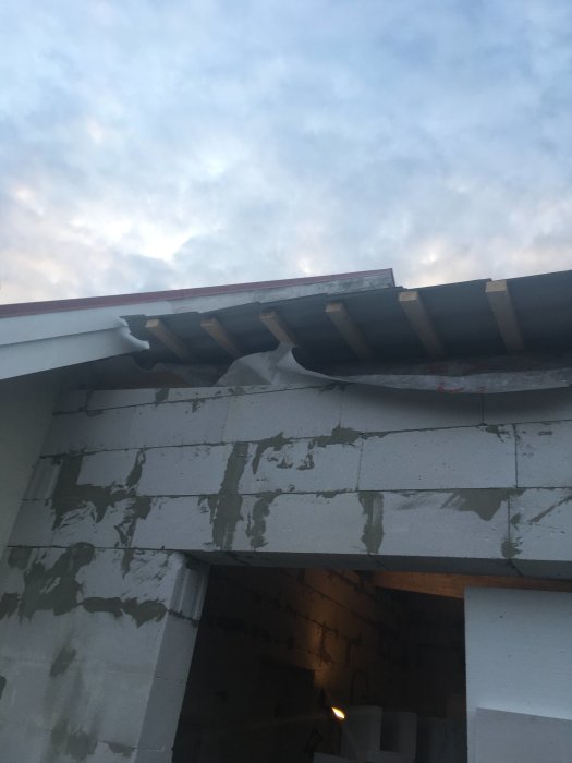 Ofärdig vindskena och takstomme på hus under konstruktion mot en himmel vid skymningen.