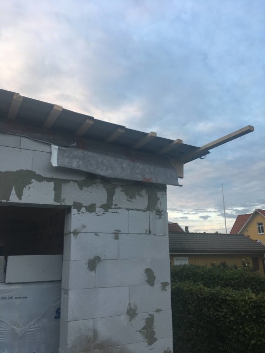 Ofärdig vindskena och takstolar på hus i konstruktion mot en tidig kvällshimmel.