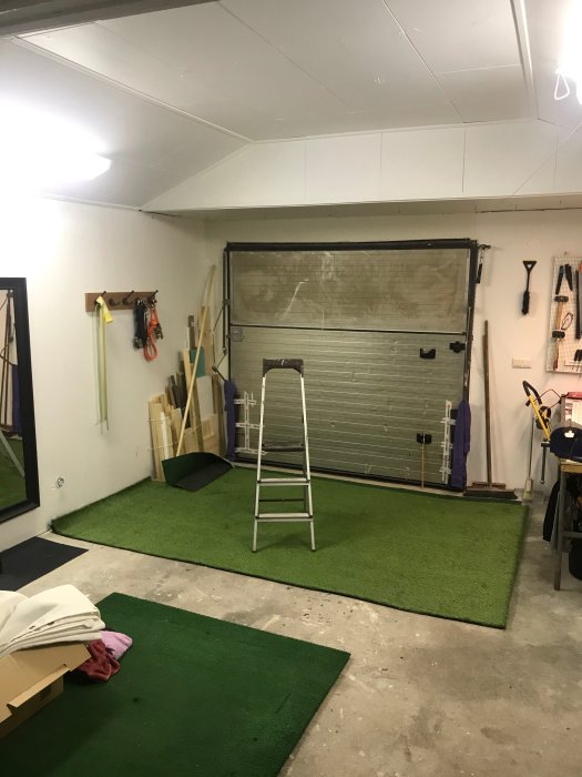 Interiör av ett garage med vitmålad takkonstruktion, ett grönt golv och en stängd garageport.