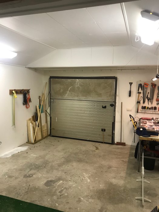 Garageinteriör med förstärkta takstolar, stängd garageport och organiserade verktyg på väggen.