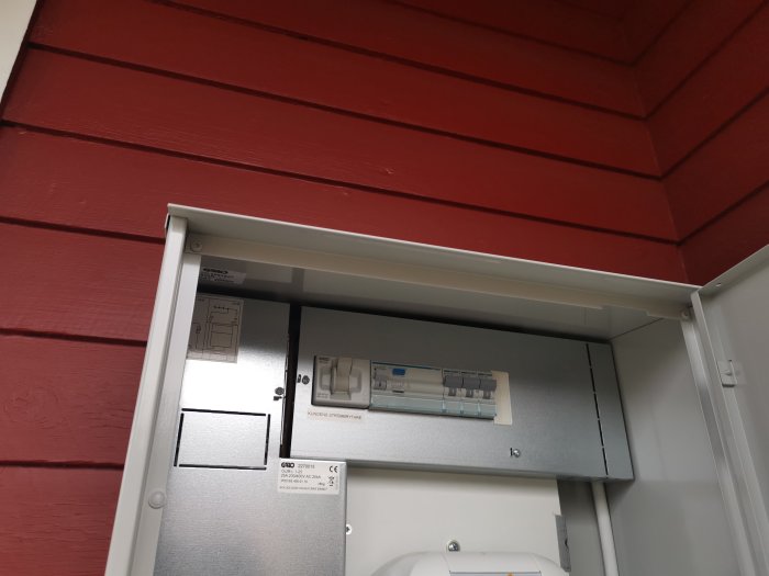 Elektrisk utrustning med jordfelsbrytare installerad på en rödmålad vägg i ett säkerhetsskåp.