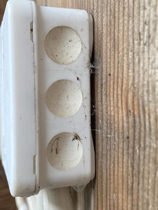Vit elkontakt med damm och spindelväv på en vägg, visar tecken på att inte öppnats på länge.