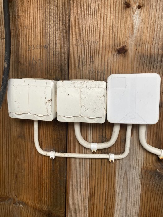 En väggmonterad elinstallation med tre äldre, smutsiga strömbrytare och synliga rör mot en trävägg.