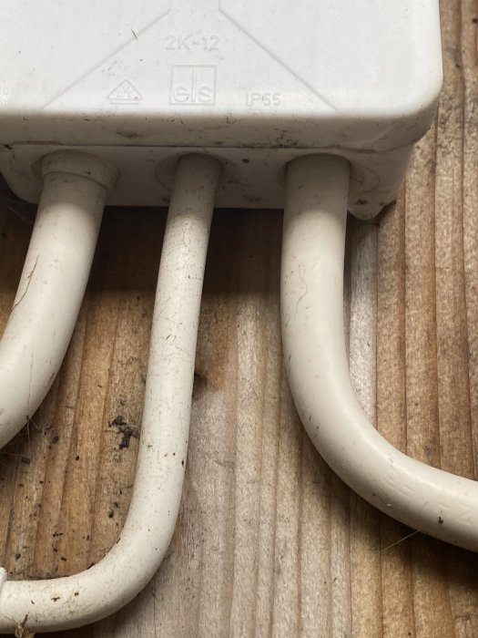 Stängd elektrisk anslutningsdosa med tre ingående kablar på ett brunt träunderlag.